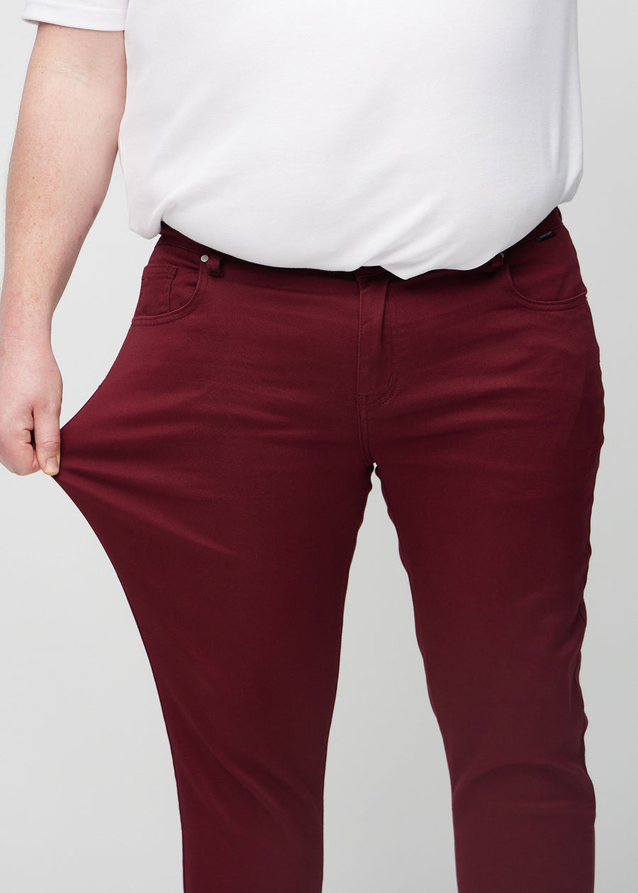 Plus-size-modell strekker jeansene ved låret for å vise materialets stretch.