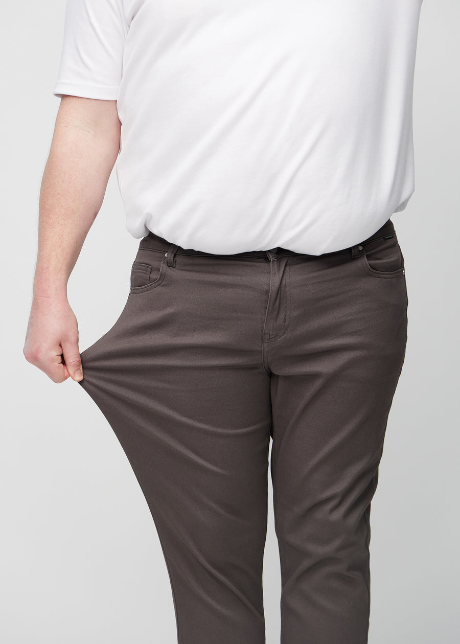 Plus-size-modell strekker jeansene ved låret for å vise materialets stretch.
