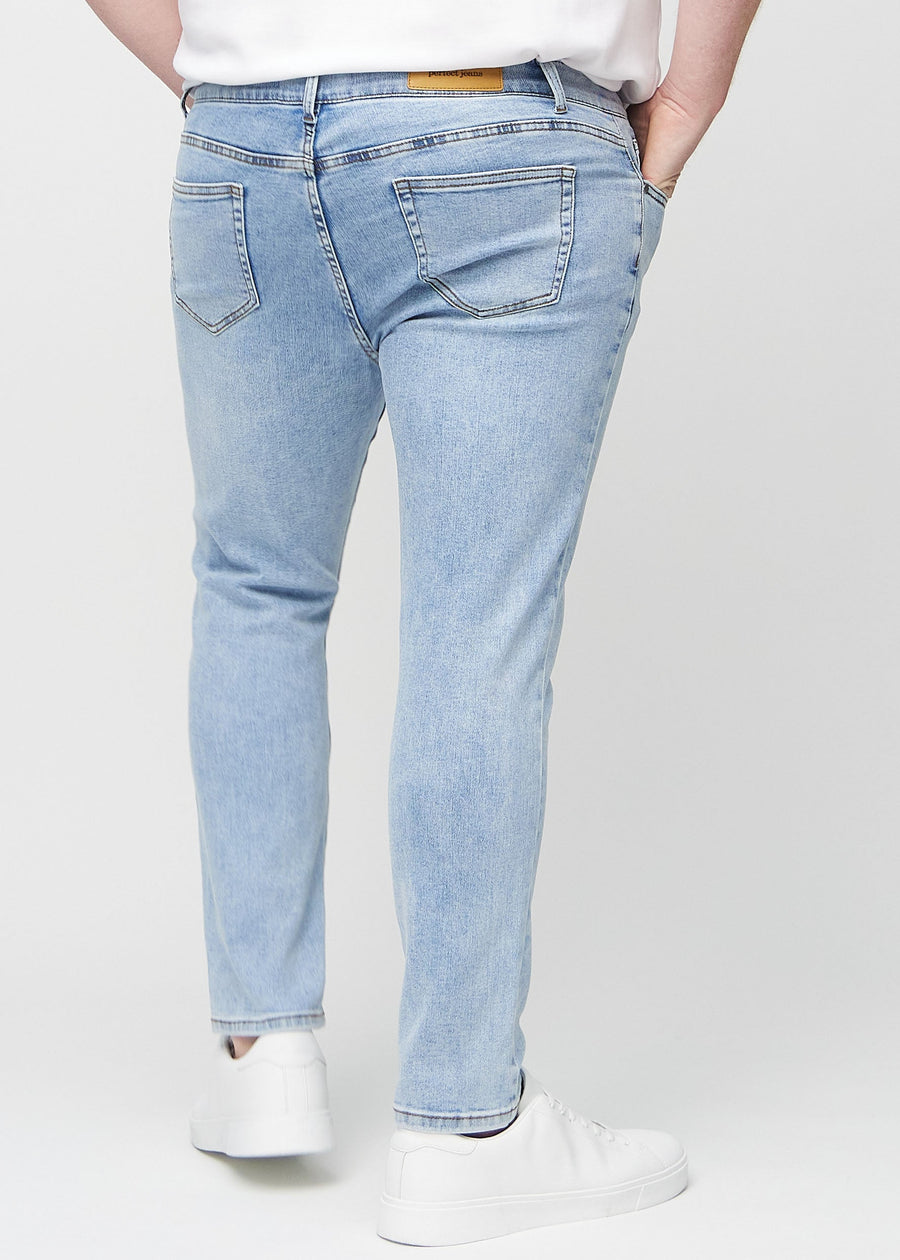 Lyseblå denimjeans i slim fit sett bakfra på en plus-size-modell for å vise hele produktet.