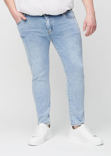 Lyseblå denimjeans i slim fit, modellnavn Waves, som sitter tett langs bena på en plus-size-modell, sett forfra.