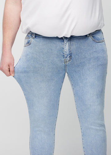 Plus-size-modell strekker jeansene ved låret for å vise materialets stretch.