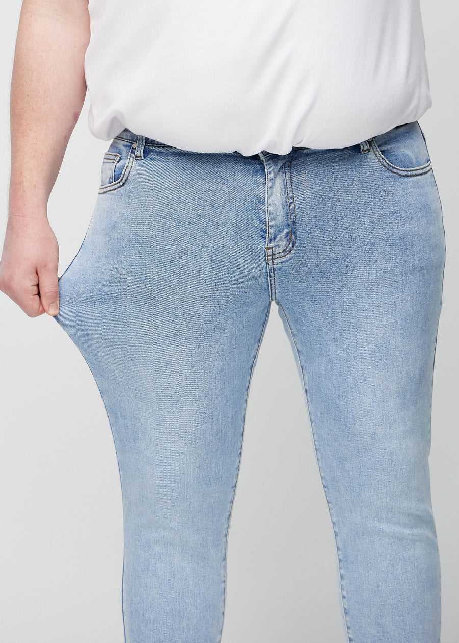 Plus-size-modell strekker jeansene ved låret for å vise materialets stretch.