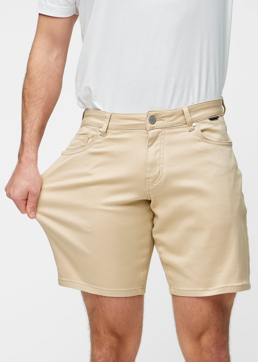 Modell strekker beige shorts til herre i fargen Gazelles ved låret for å vise materialets stretch.