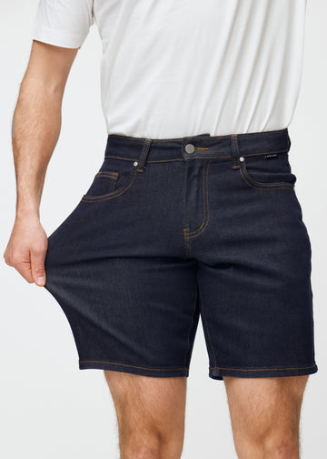 modell strekker dyp mørkeblå denimshorts til herre i fargen midnights ved låret for å vise materialets stretch.