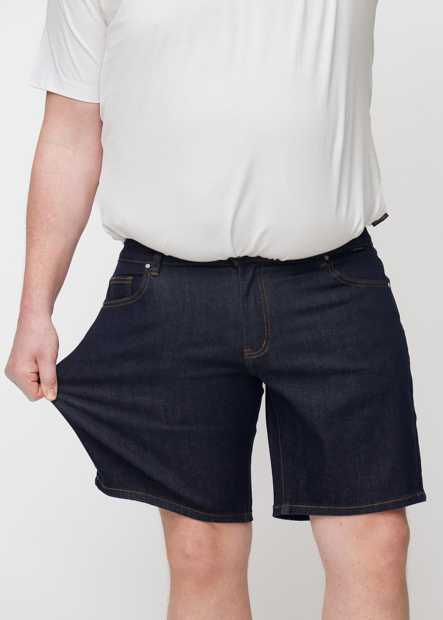 plus-size modell strekker dyp mørkeblå denimshorts til herre i fargen midnights ved låret for å vise stretch.