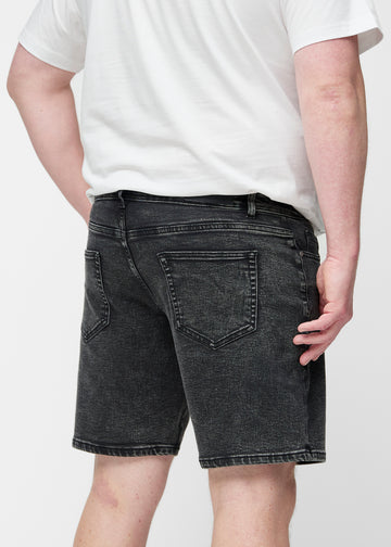 Plus-size modell strekker mørkegrå denimshorts til herre i fargen Shadows ved låret for å vise materialets stretch.