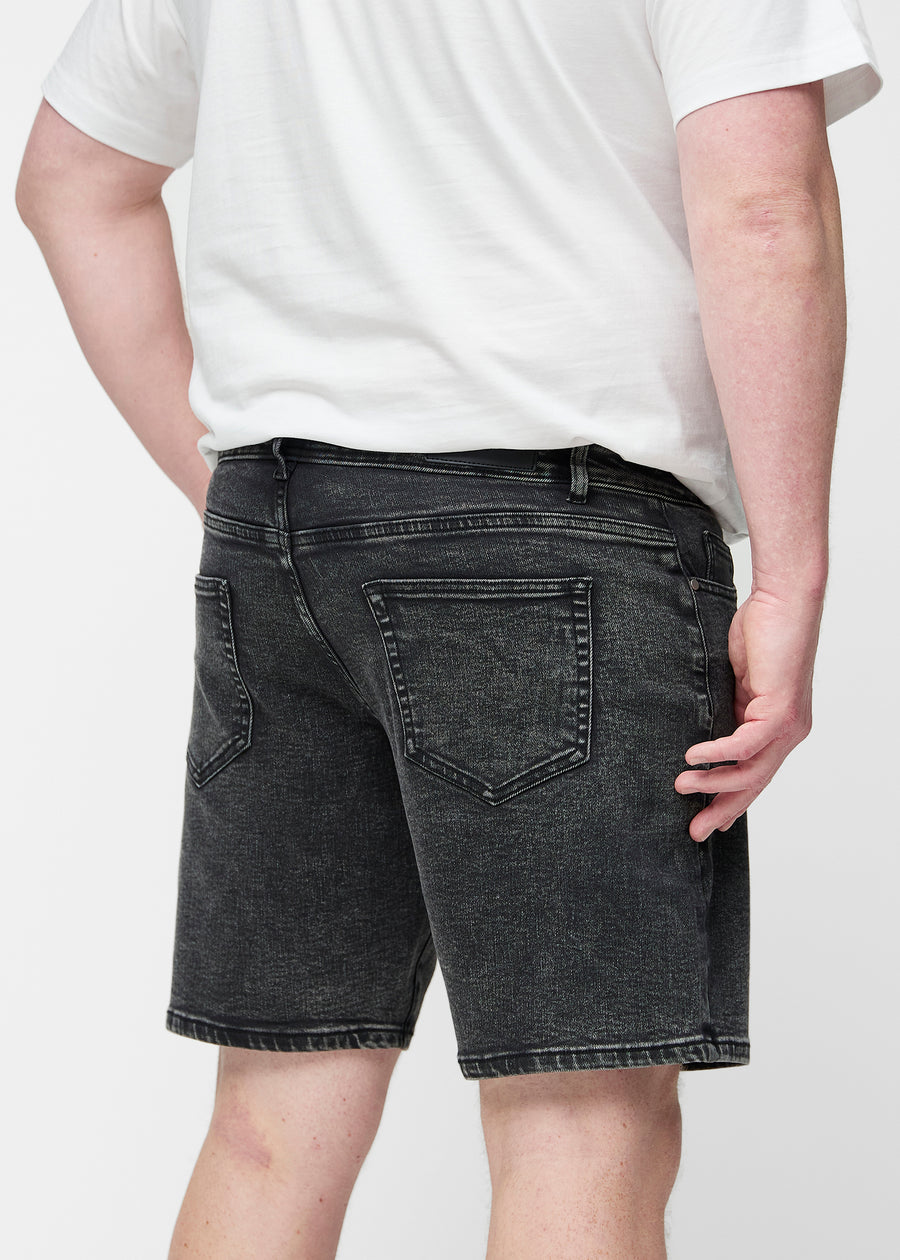 Plus-size modell strekker mørkegrå denimshorts til herre i fargen Shadows ved låret for å vise materialets stretch.