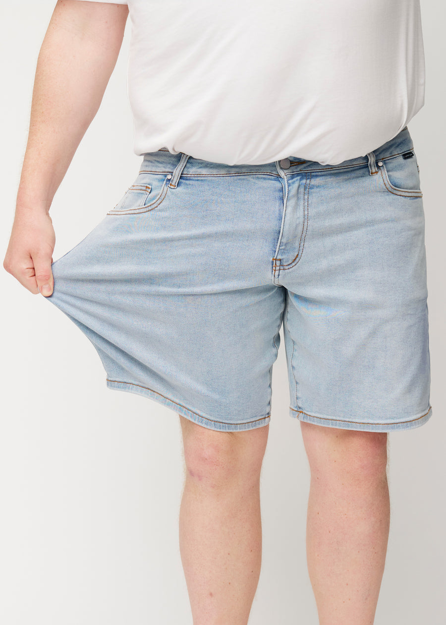 Plus-size-modellen strekker lyseblå denimshorts til menn i fargen Waves ved låret for å vise materialets stretch.