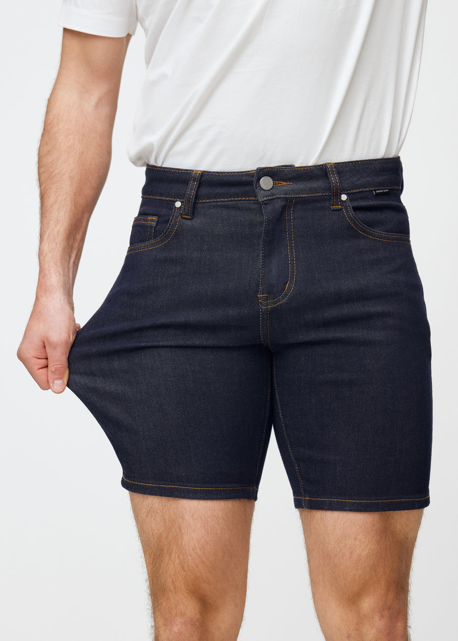 Modell strekker dyp mørkeblå denimshorts til herre i fargen Midnights ved låret for å vise materialets stretch.