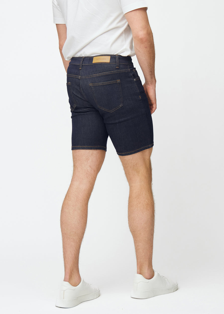 Dyp mørkeblå denimshorts til herre i fargen Midnights sett bakfra, slik at lengden rett over kneet vises.