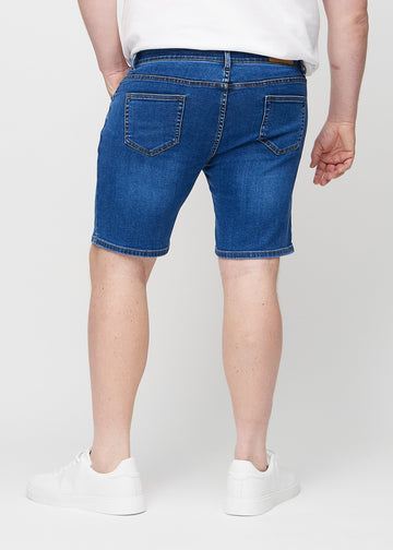Mørke denim middle-slim shorts sett bakfra på en plus-size-modell, så man kan se hele produktet.