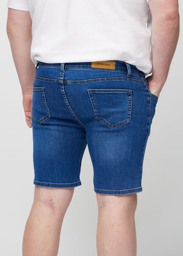 Mørke denim middle-slim shorts sett bakfra på nært hold på en plus-size-modell for å vise detaljer.