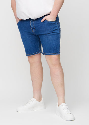 Mørke denim middle-slim shorts, som sitter rett langs låret og slutter rett over kneet på en plus-size-modell, sett forfra.