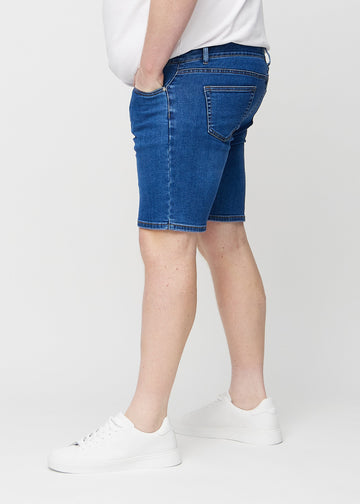 Mørke denim middle-slim shorts sett fra siden på en plus-size-modell.