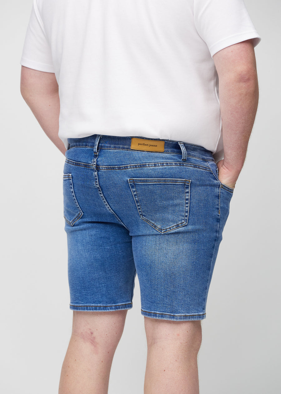Denim middle-slim shorts sett bakfra på nært hold på en plus-size-modell for å vise detaljer.
