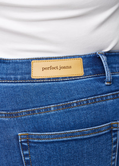 Baglommen på et par mørkeblå denim slim capris set tæt på – tydeligt logo og tekstur vist på en plus-size model.