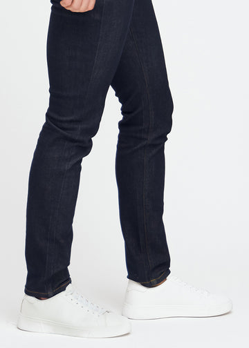 Dyp mørkeblå denimjeans for menn i fargen Midnights med slim passform, vist på nært hold ved anklene for å fremheve den smale benavslutningen.