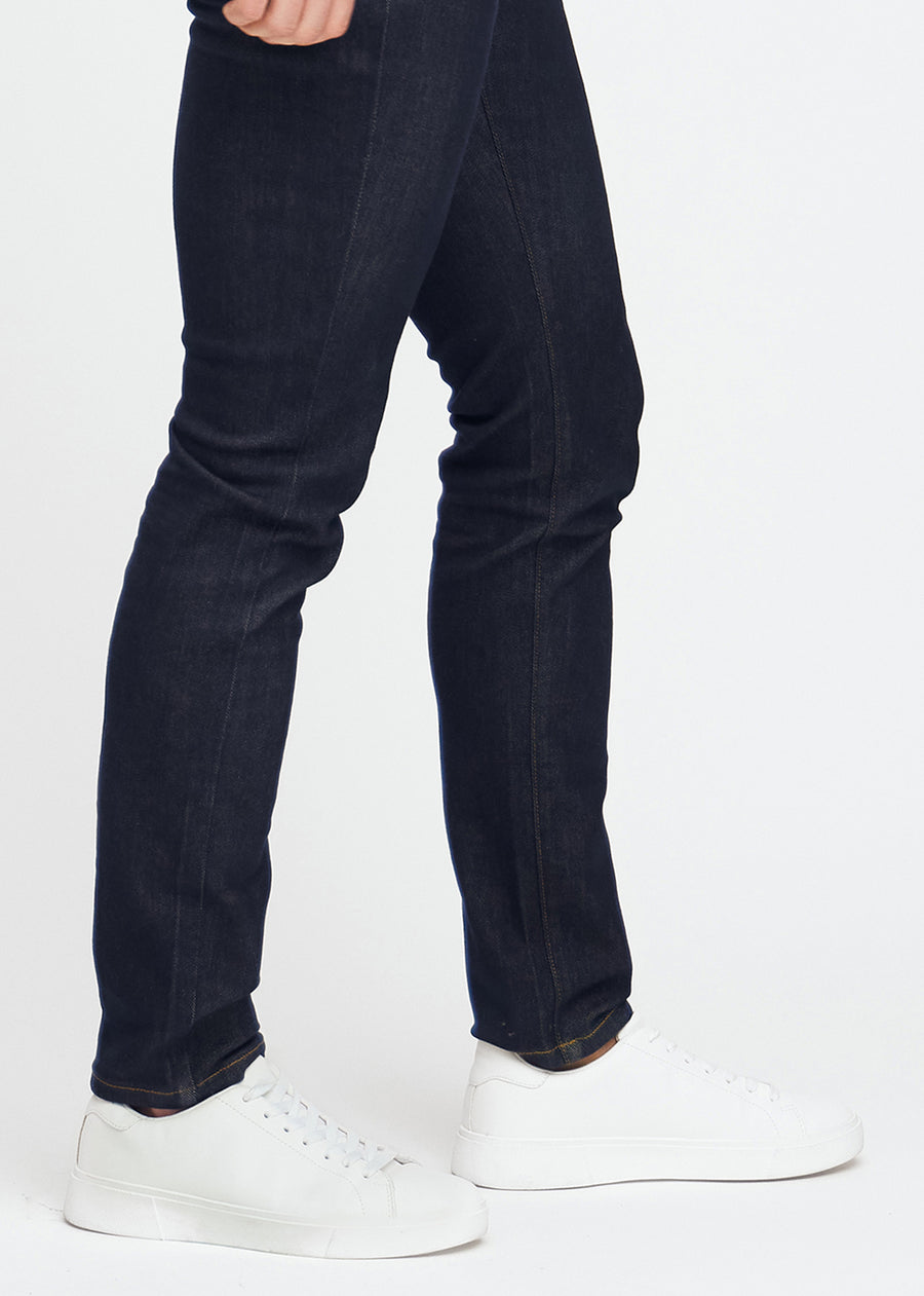 Dyp mørkeblå denimjeans for menn i fargen Midnights med slim passform, vist på nært hold ved anklene for å fremheve den smale benavslutningen.