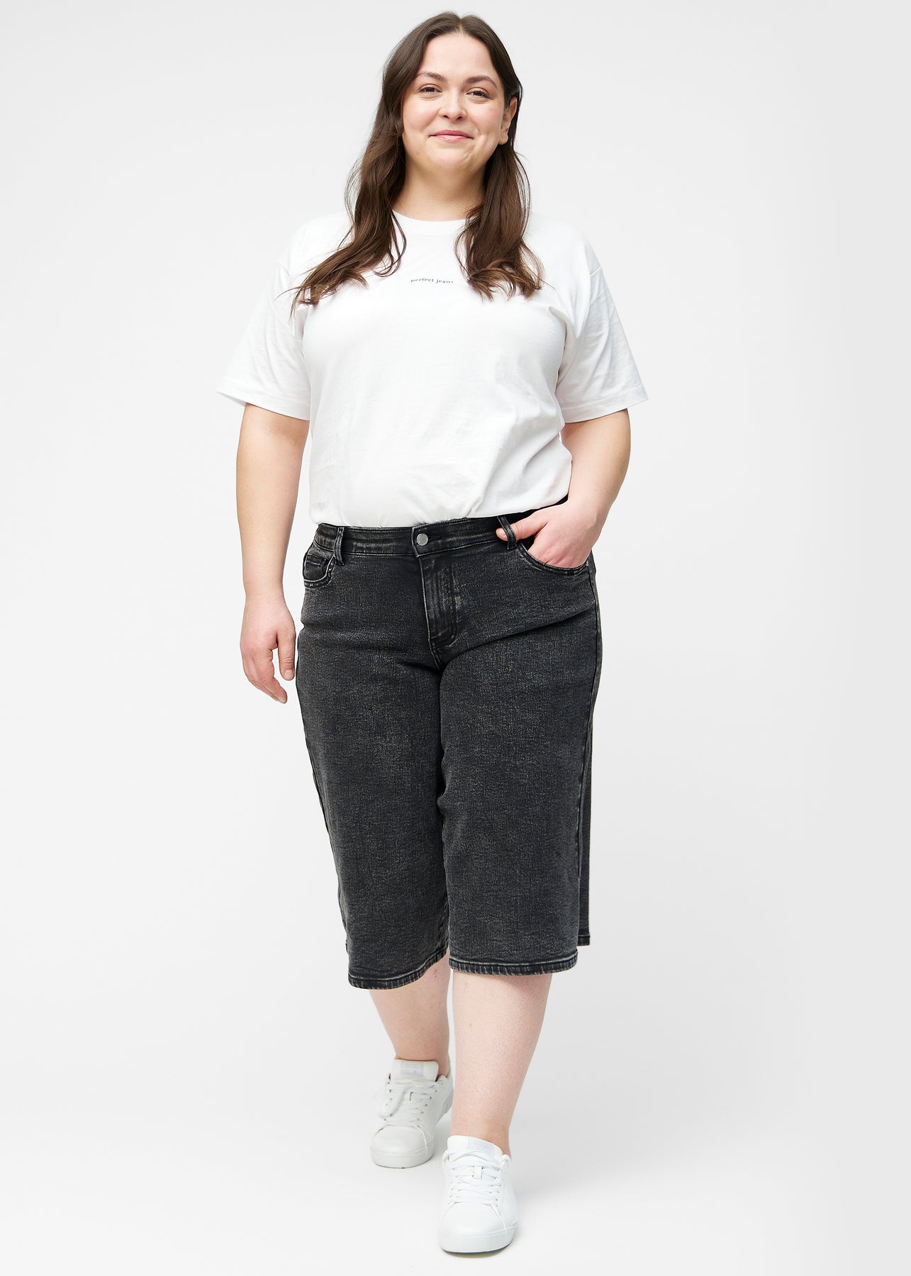 Plus-size model viser løse, mørkegrå denim capris i farven Shadows i bevægelse og demonstrerer pasform og materiale.