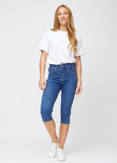 Model træder ind i billedet, strækker i sine mørkeblå denim slim capris, viser dem frem ved at dreje rundt, og går derefter ud af billedet igen.